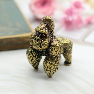 May include: A small, gold-colored figurine of a gorilla. The figurine is detailed with textured fur and has a realistic appearance.