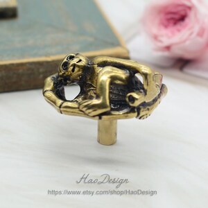 Puede incluir: Pomo de armario de mono dorado con un dise&ntilde;o detallado. El mono est&aacute; sentado en una base redonda con un dise&ntilde;o decorativo. El pomo est&aacute; unido a un poste de metal.