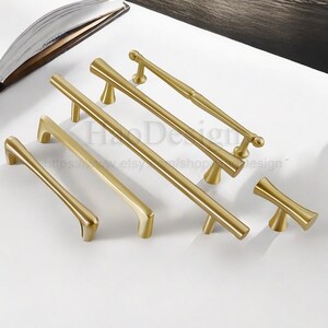 Puede incluir: Una colecci&oacute;n de tiradores y manijas doradas para gabinetes en varios tama&ntilde;os y dise&ntilde;os. El hardware incluye tiradores de barra y manijas tipo pomo, todos con una est&eacute;tica elegante y moderna. Las piezas est&aacute;n dispuestas sobre una superficie blanca.