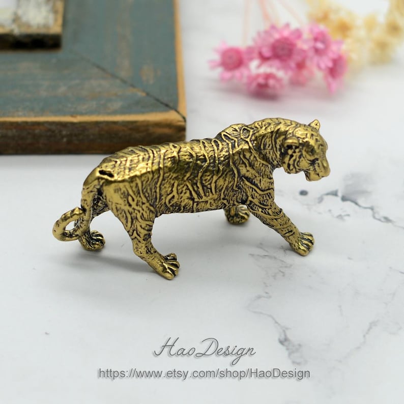 Pode incluir: Uma figurinha de metal dourada de um tigre caminhando. O tigre tem uma pelagem detalhada e uma cauda enroscada.