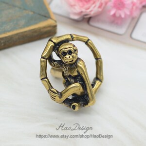 Puede incluir: Una figurita de mono dorada sujetando un anillo de bamb&uacute;. El mono est&aacute; sentado en una rama y tiene una cara detallada.