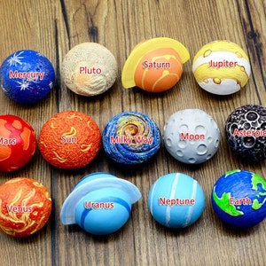 May include: A collection of colorful planet and celestial body models, including Mercury, Pluto, Saturn, Jupiter, Mars, the Sun, the Milky Way, the Moon, an Asteroid, Venus, Uranus, Neptune, and Earth. Each model is labeled with its name.