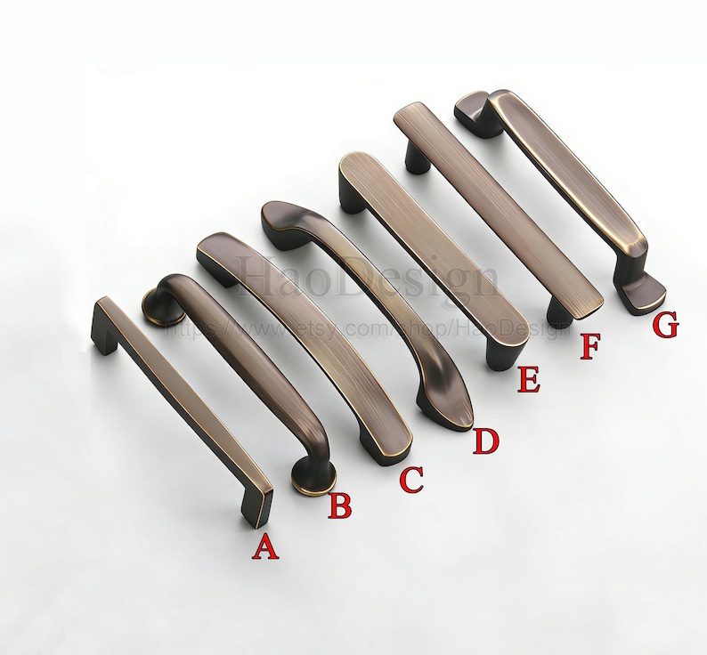 May include: A selection of seven antique bronze cabinet pulls in different styles. The pulls are arranged at an angle, displaying their diverse shapes and finishes. Each pull is labelled with a letter from A to G.