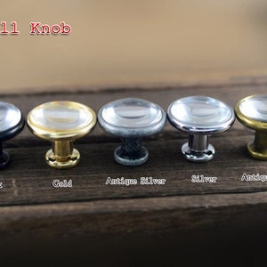 以下が含まれることがあります： 黒、金、アンティークシルバー、シルバー、アンティークブロンズなど、さまざまな仕上げの金属製ベースが付いた、小さな丸いガラス製のノブが5つあります。  "Small Knob"という文字がノブの上に書かれています。