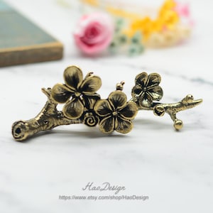 May include: A gold-toned metal hair clip shaped like a branch with three delicate cherry blossom flowers. The flowers have five petals each and are arranged along the branch.