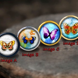 May include: Four round glass cabochons with different butterfly designs. The cabochons are set in metal settings. The butterflies are in various colours, including blue, purple, orange, and yellow. The cabochons are labelled Image A, Image B, Image C, and Image D.