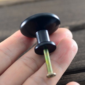 以下が含まれることがあります： 丸くて滑らかな表面と銀色のネジが付いた黒いキャビネットノブ。