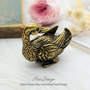 May include: A small, gold-coloured metal duck figurine with detailed feathers and a textured surface.