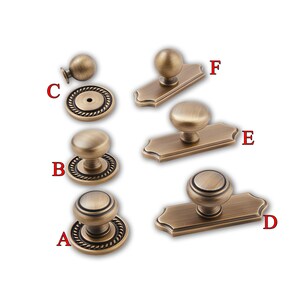 May include: An assortment of antique bronze cabinet hardware, including knobs and pulls. The knobs have a round shape, while the pulls are mounted on rectangular backplates. The hardware is designed for cabinets and drawers.