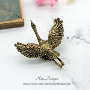 May include: A gold-toned metal crane figurine with its wings spread wide. The crane is in flight and has a detailed design.