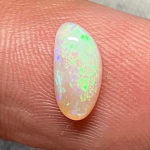 May include: A small, oval-shaped opal gemstone with a white base and iridescent green, blue, and purple flashes.