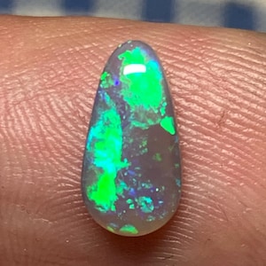 May include: A teardrop-shaped opal gemstone with a light grey base and flashes of green, blue, and purple.