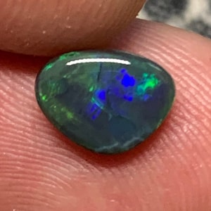 May include: A dark green, blue, and black opal gemstone with a teardrop shape.