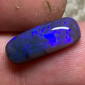 May include: An oval-shaped opal gemstone, dark blue and black in colour, with iridescent flashes of colour.