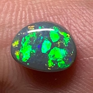 May include: A dark grey cabochon opal with green and blue flashes of colour.