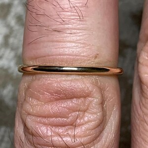 Puede incluir: Un anillo de banda de oro delgado usado en un dedo.