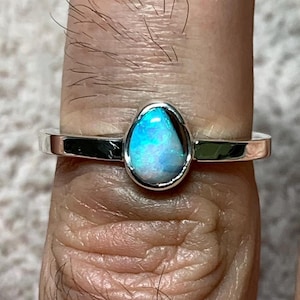 May include: A silver ring with a teardrop-shaped opal gemstone. The opal is a light blue color with flashes of iridescent color.