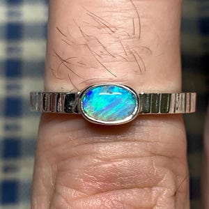 May include: A silver ring with a blue opal gemstone. The ring has a textured band.