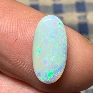 May include: Oval-shaped white opal gemstone with green and blue iridescent flashes.
