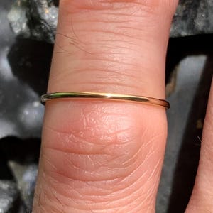 Peut inclure: Une fine bague de couleur or. La bague est de conception simple, probablement en or ou en métal doré. La bague est présentée sur un doigt, soulignant son style délicat et minimaliste. La surface lisse de la bague reflète la lumière, lui donnant un aspect poli.
