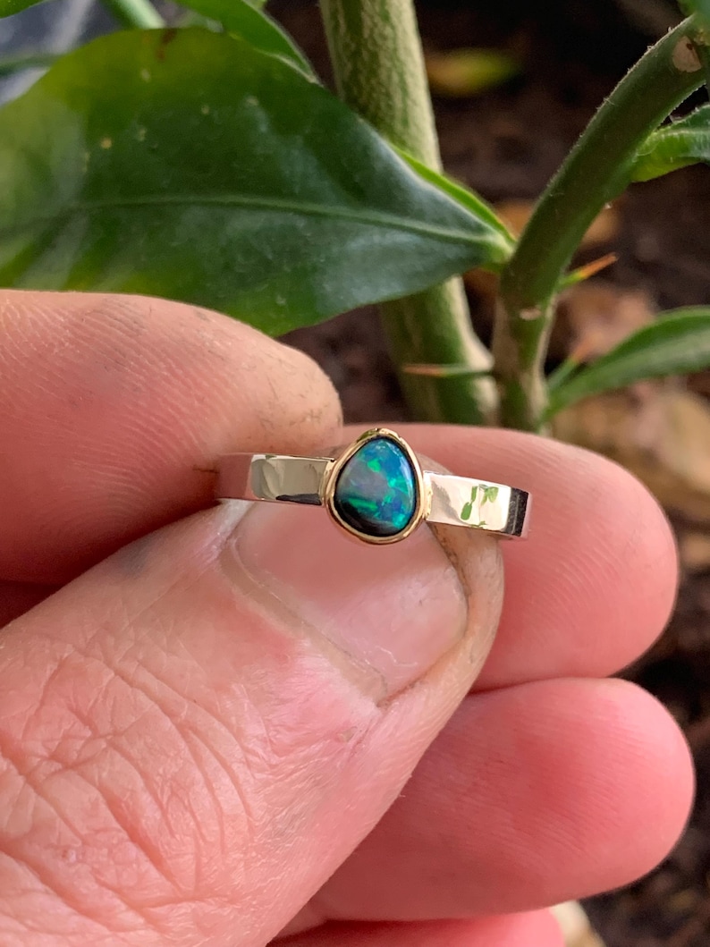 May include: A gold-toned ring with a teardrop-shaped opal gemstone. The opal has a dark blue and green color with a gold bezel setting. The ring band is a simple, polished design.