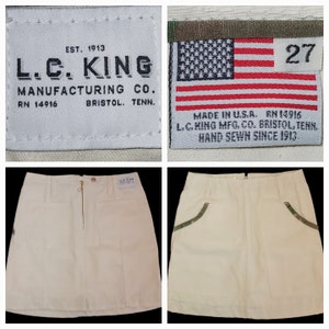 May include: A white denim mini skirt with a zipper closure and a camouflage trim. The skirt has a label that reads "L.C. King Manufacturing Co. RN 14916 Bristol, Tenn."