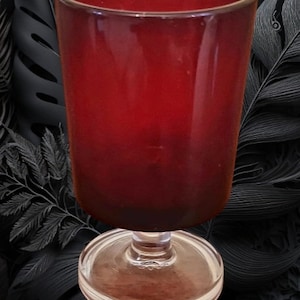May include: A tall, clear glass with a red, opaque base and a clear, round pedestal base. The glass is empty.