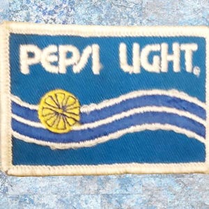 May include: A blue and white embroidered patch with the text "Pepsi Light" and a yellow lemon design.