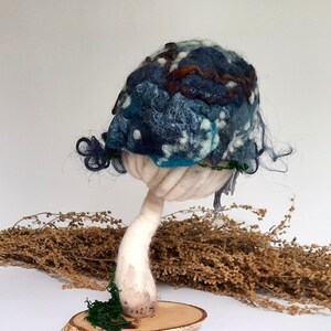 Könnte beinhalten: Ein blauer und weißer Filzpilz mit einem weißen Stiel, der auf einem Holzsockel mit grünem Moos steht.