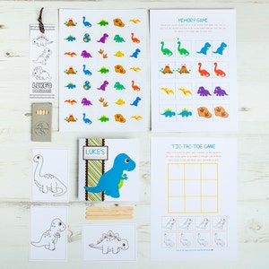 May include: A set of dinosaur-themed party games for kids. The set includes a memory game, a tic-tac-toe game, coloring pages, and stickers. The games are printed on white cardstock and feature colorful illustrations of dinosaurs.