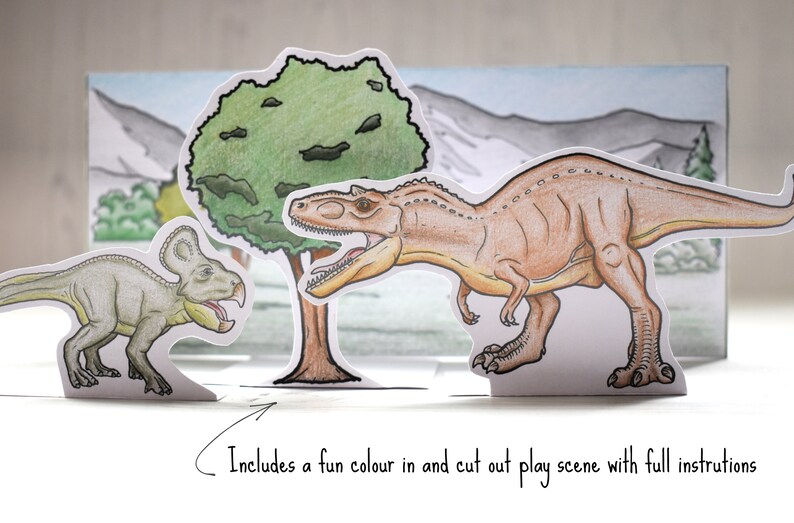 Op de afbeelding: Een papieren knutselspel met twee dinosaurussen, een groene boom en een bergketen. De dinosaurussen zijn een bruine Tyrannosaurus Rex en een groene Triceratops. De sc&egrave;ne is ontworpen om in te kleuren en uit te knippen.