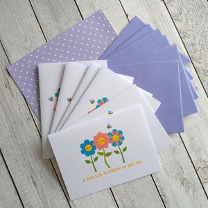 May include: Set of six blank greeting cards featuring colourful flower illustrations and the text "A little note to brighten up your day". The cards come with six matching lavender envelopes with a white polka dot pattern.