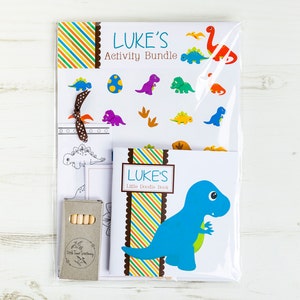 May include: A dinosaur-themed activity bundle for kids named "LUKE'S Activity Bundle". The bundle includes a coloring book, a sticker sheet, and a set of crayons. The coloring book features a blue dinosaur with a green leaf in its mouth. The sticker sheet has a variety of colorful dinosaurs and footprints. The crayons are brown and have a label that says "Little Twigs Stationery".
