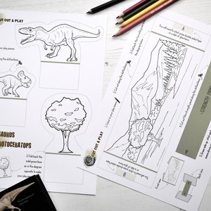 Op de afbeelding: Een zwart-witte printbare knip- en speelactiviteit met een Gorgosaurus- en een Protoceratops-dinosaurus, een boom en een berglandschap. De instructies zijn om de speelstukken in te kleuren, langs de stippellijnen te knippen en de flappen terug te vouwen om de speelstukken rechtop te laten staan.