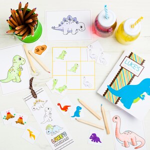 May include: A set of dinosaur-themed coloring pages and a bookmark with the text "Luke's Bookmark". The pages feature various dinosaurs, including a green dinosaur, a blue dinosaur, and a pink dinosaur. There are also some crayons and a cup of colored pencils.