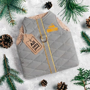 May include: Gray quilted dog vest with a yellow trim and a cork fabric backing. The vest has a D-ring and a tag that says "All cats food".