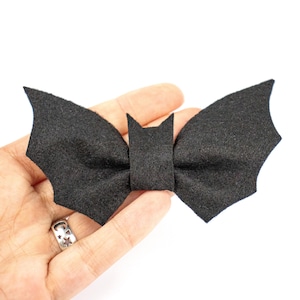 Könnte beinhalten: Eine schwarze Filzschleife in Form einer Fledermaus. Die Schleife ist in der Mitte gebunden und hat zwei Flügel, die wie Fledermausflügel geformt sind.