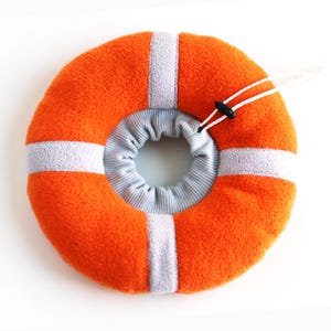 Può includere: Collare di recupero per animali domestici morbido di colore arancione e grigio. Il collare ha la forma di un ciambellone ed è dotato di un cinturino bianco regolabile.