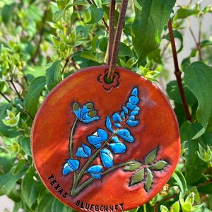 May include: A round, brown leather ornament with a bluebonnet flower design and the text "Texas Bluebonnet".