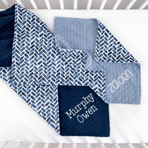 K&ouml;nnte beinhalten: Eine Patchwork-Babydecke mit einem marineblauen und wei&szlig;en Aquarell-Fischgr&auml;tenmuster, einem einfarbigen marineblauen Abschnitt und einem hellblauen Abschnitt. Die Decke ist mit den Namen "Zaidan" und "Murphy Owen" in Wei&szlig; bestickt.