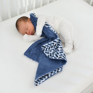 K&ouml;nnte beinhalten: Ein schlafendes Baby liegt in einem wei&szlig;en Kinderbett und ist in eine weiche, blaue Decke geh&uuml;llt. Die Decke hat ein Aquarell-Ziegelmuster in Blau- und Wei&szlig;t&ouml;nen. Die Decke ist aus einem Pl&uuml;schmaterial gefertigt.