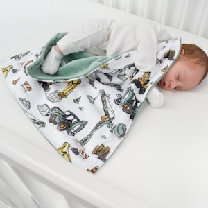 May include: A white and green baby blanket with a construction theme. The blanket features a variety of construction vehicles, including trucks, cranes, and bulldozers. The blanket is made of soft, comfortable fabric and is perfect for cuddling.