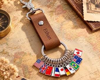 May include: A brown leather keychain featuring a silver metal lobster clasp and a ring adorned with multiple small rectangular enamel charms representing various national flags. The leather strap is embossed with the name Ethan in a dark font.