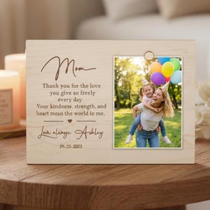 Può includere: Cornice in legno con una foto di una donna e un bambino, e la parola "Mamma" e un messaggio d'amore. La cornice include la data "04.25.2023" ed è su una superficie di legno.