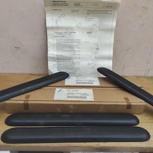 May include: A set of four black Honda bumper corner protectors with an original installation instruction sheet. The kit includes two long, curved pieces and two shorter, straight pieces, all packaged with a cardboard box and technical diagrams.