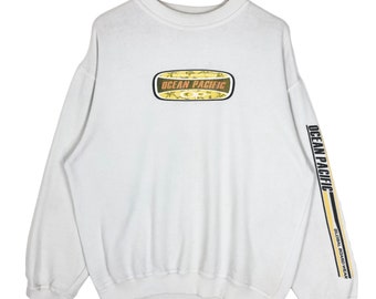 May include: White sweatshirt with the text "OCEAN PACIFIC" in a rectangular design on the front. The right sleeve has the text "OCEAN PACIFIC" and a yellow stripe. The sweatshirt is hanging on a wooden hanger.