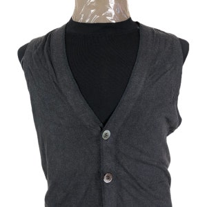 May include: A dark gray, button-down vest with a V-neck. The vest has two buttons and is displayed on a black mannequin. The vest is made of a soft, possibly knit, material.