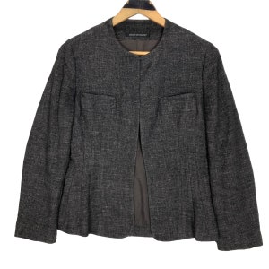 May include: A dark grey blazer with a textured weave, featuring a round collar and two small front pockets. The jacket is open at the front and hangs on a wooden hanger.