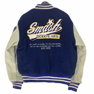 May include: A navy blue and cream varsity jacket with the word "Smash" and "DOKKYO UNIV." embroidered on the back. The jacket has cream-colored sleeves and striped cuffs. The text "EST.1978" is also visible.