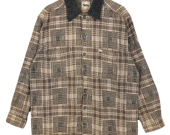 May include: A brown and beige plaid flannel shirt with a gray collar. The long-sleeved shirt has a button-down front, two chest pockets, and a small logo on the pocket. The shirt is hanging on a wooden hanger.